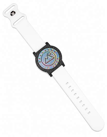 Recovewrist milestone band in white, worn watch-style with the iridescent ‘Recovery Is Cool’ recovery coin in a speckled granite bezel — made in Colorado