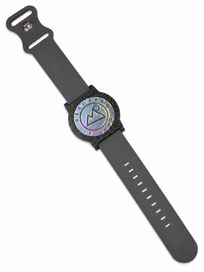 Recovewrist milestone band in grey, worn watch-style with the iridescent ‘Recovery Is Cool’ recovery coin in a speckled granite bezel — made in Colorado